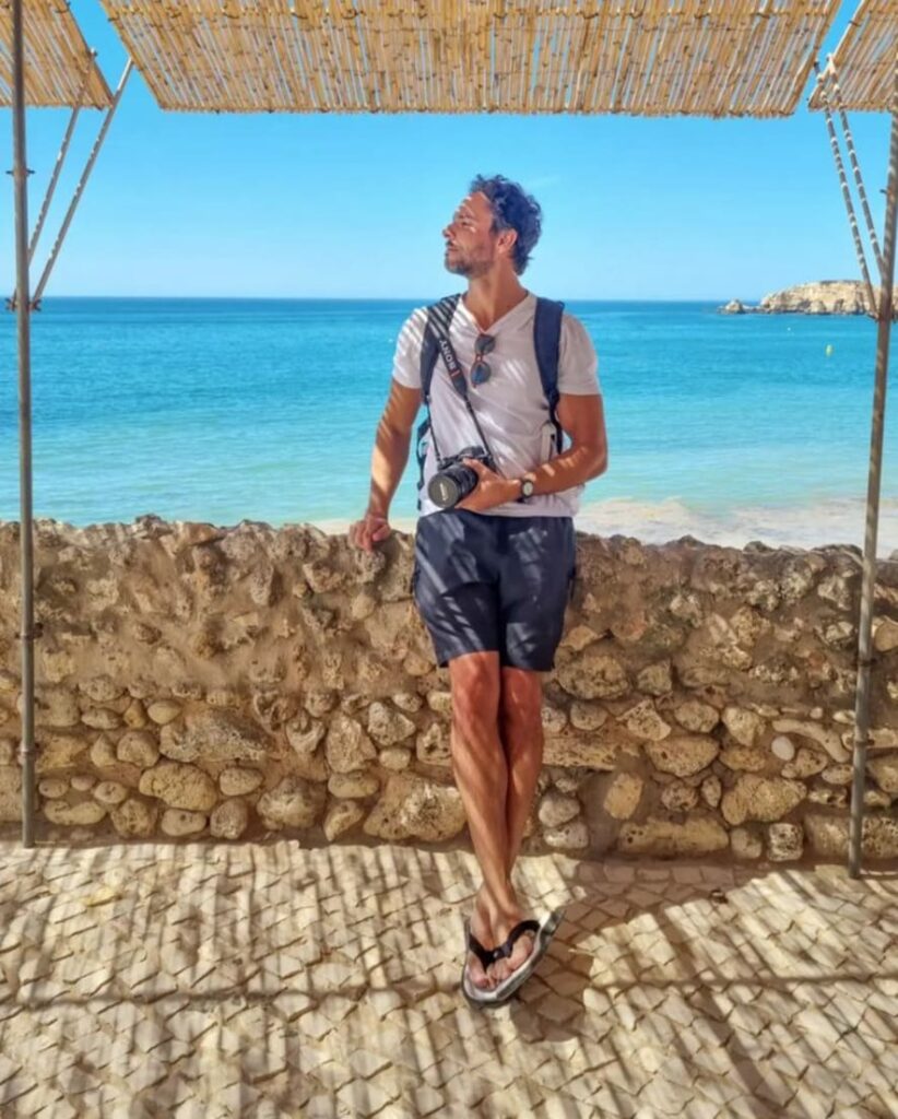 Fotógrafo Berlemes encostado em um muro de pedras na Praia do Vau